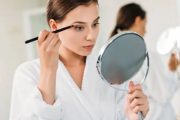 Beautiful Young Woman Holding Mirror Applying Eyeshadow — стоковое фото