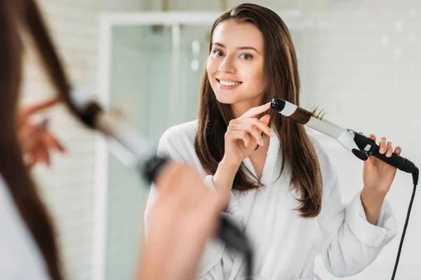 Happy Brunette Girl Bathrobe Using Hair Curler Mirror Bathroom — стоковое фото