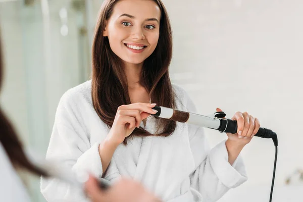 Smiling Young Woman Bathrobe Using Hair Curler Bathroom — стоковое фото